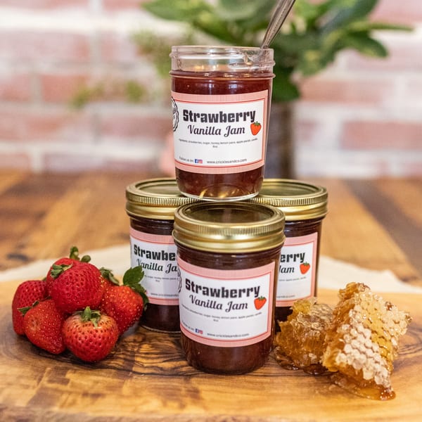 Strawberry vanilla jam jars, fresh strawberries, and honeycomb on a wooden board.