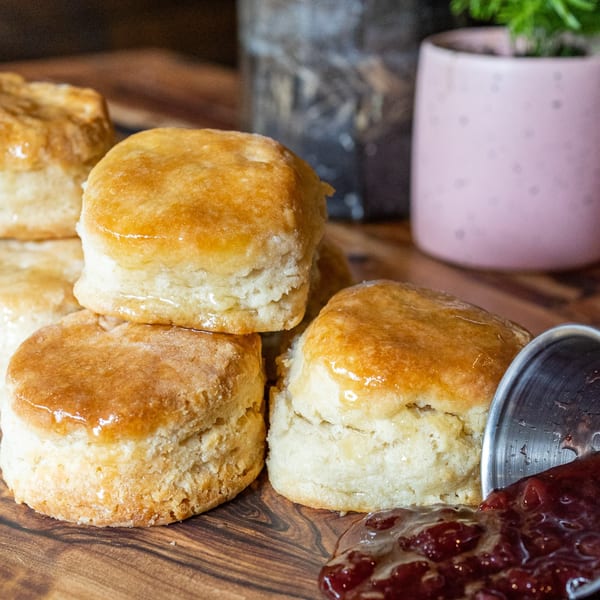 Golden brown biscuits with honey glaze and a dollop of strawberry jam on a wooden board.