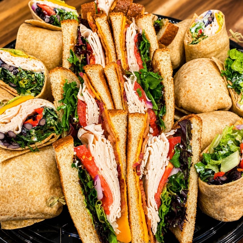 A catering platter filled with an assortment of turkey sandwiches and wraps, cut in half.