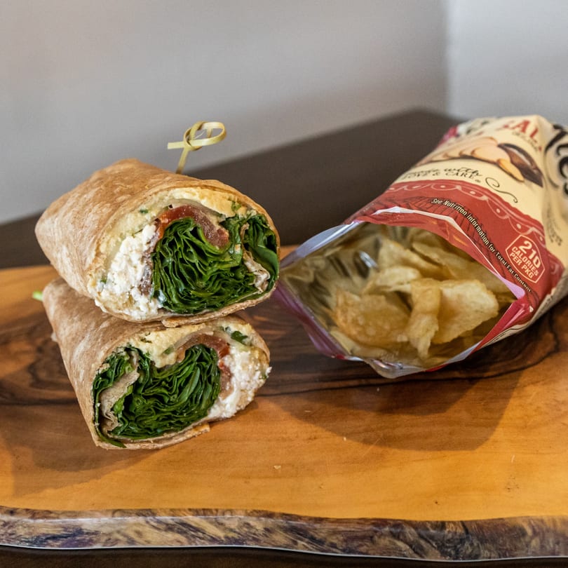 A sliced wrap filled with lettuce, cheese, and meat, next to an open bag of chips.