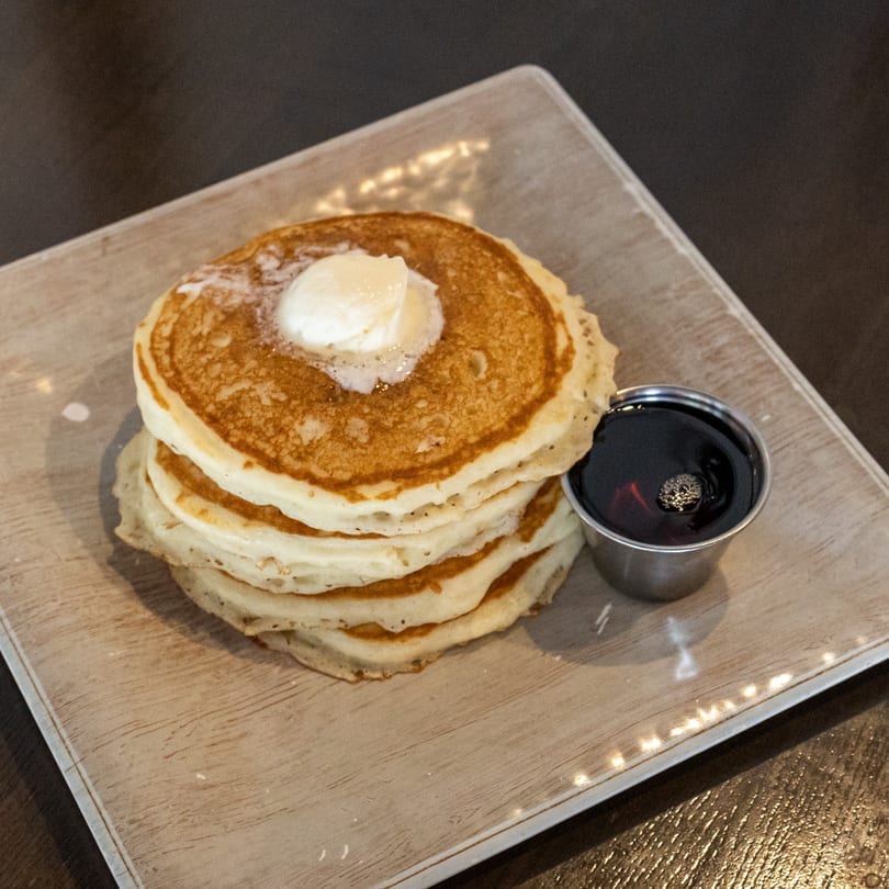 Stack of golden pancakes topped with melting butter, served with a side of maple syrup.