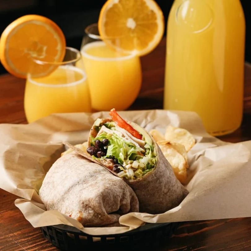 A chicken and black bean wrap with chips, served with orange juice and a bottle of juice.