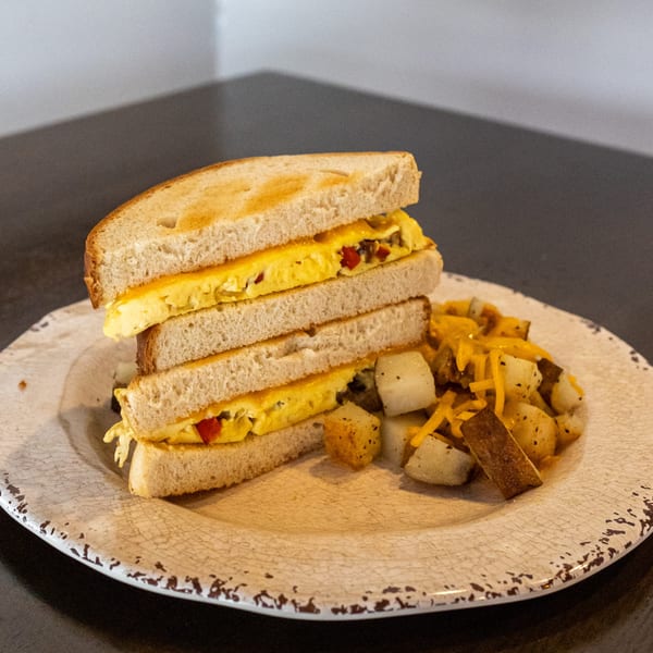 Breakfast sandwich with scrambled eggs, red peppers, and cheese, served with seasoned potatoes.