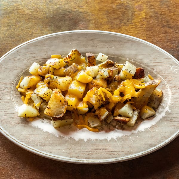 Close-up of a plate of cheesy breakfast potatoes, seasoned with pepper, on a rustic white plate.