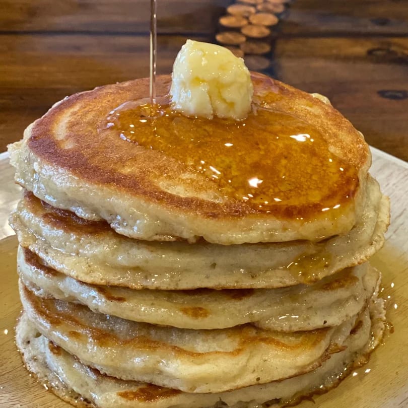 A stack of five golden pancakes with melting butter and syrup drizzling down.