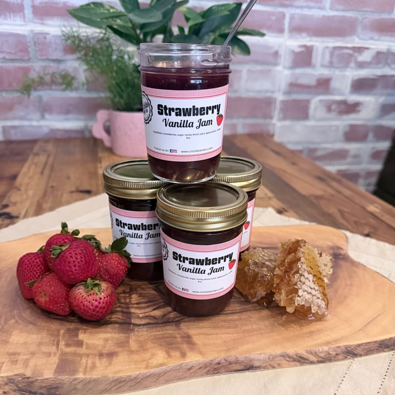 Strawberry Vanilla Jam jars, fresh strawberries, and honeycomb on a wooden board.