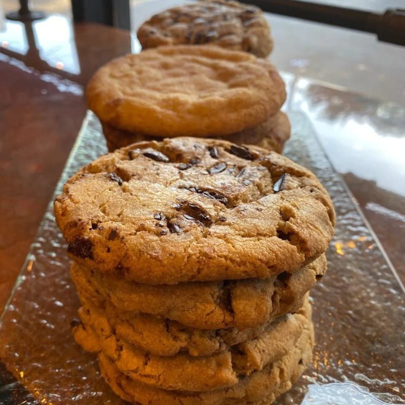 A stack of freshly baked chocolate chip cookies on a clear glass tray.